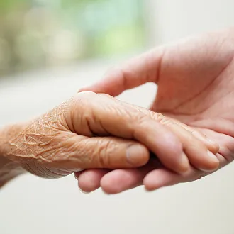 Two hands clasped, symbolizing care and connection between generations, with a blurred green background.